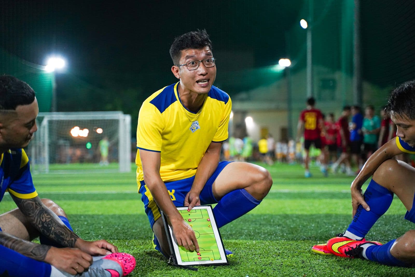 A coach talks tactics with his squad at a floodlit night session