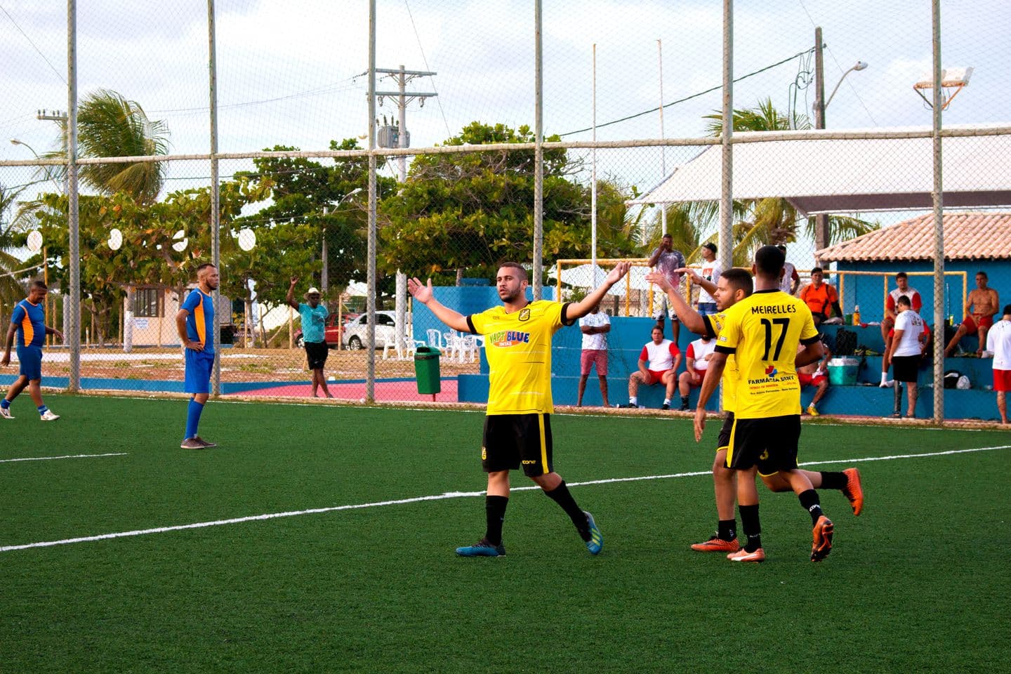 Amateur footballers in yellow jerseys celebrate a goal on a grass pitch