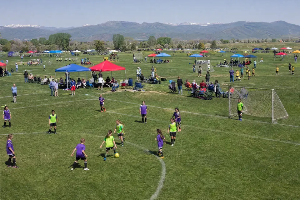 Youth soccer tournament day seen from above, several small-sided games on adjacent pitches with team tents along the touchline